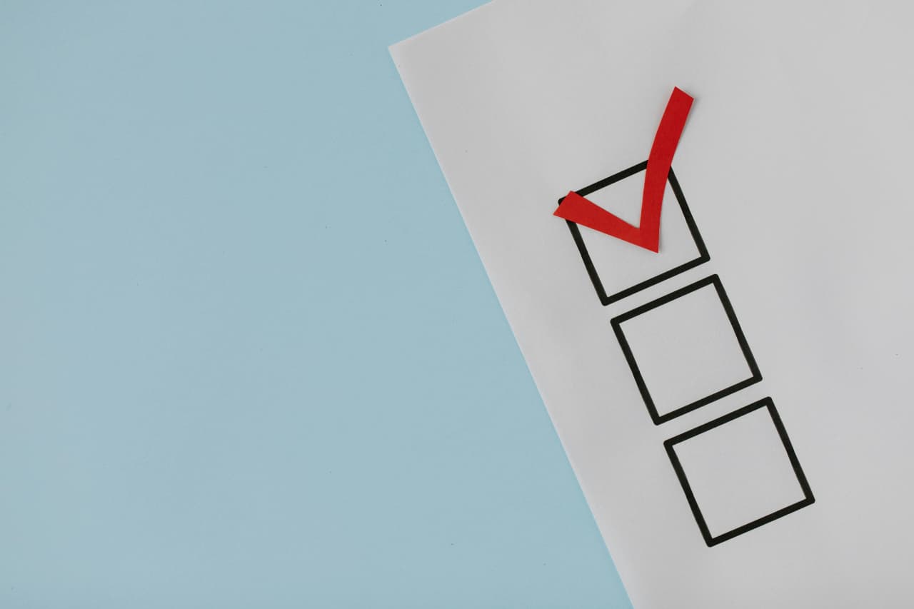 Close-up of a paper checklist with a bold red checkmark in one box, placed on a light blue background.