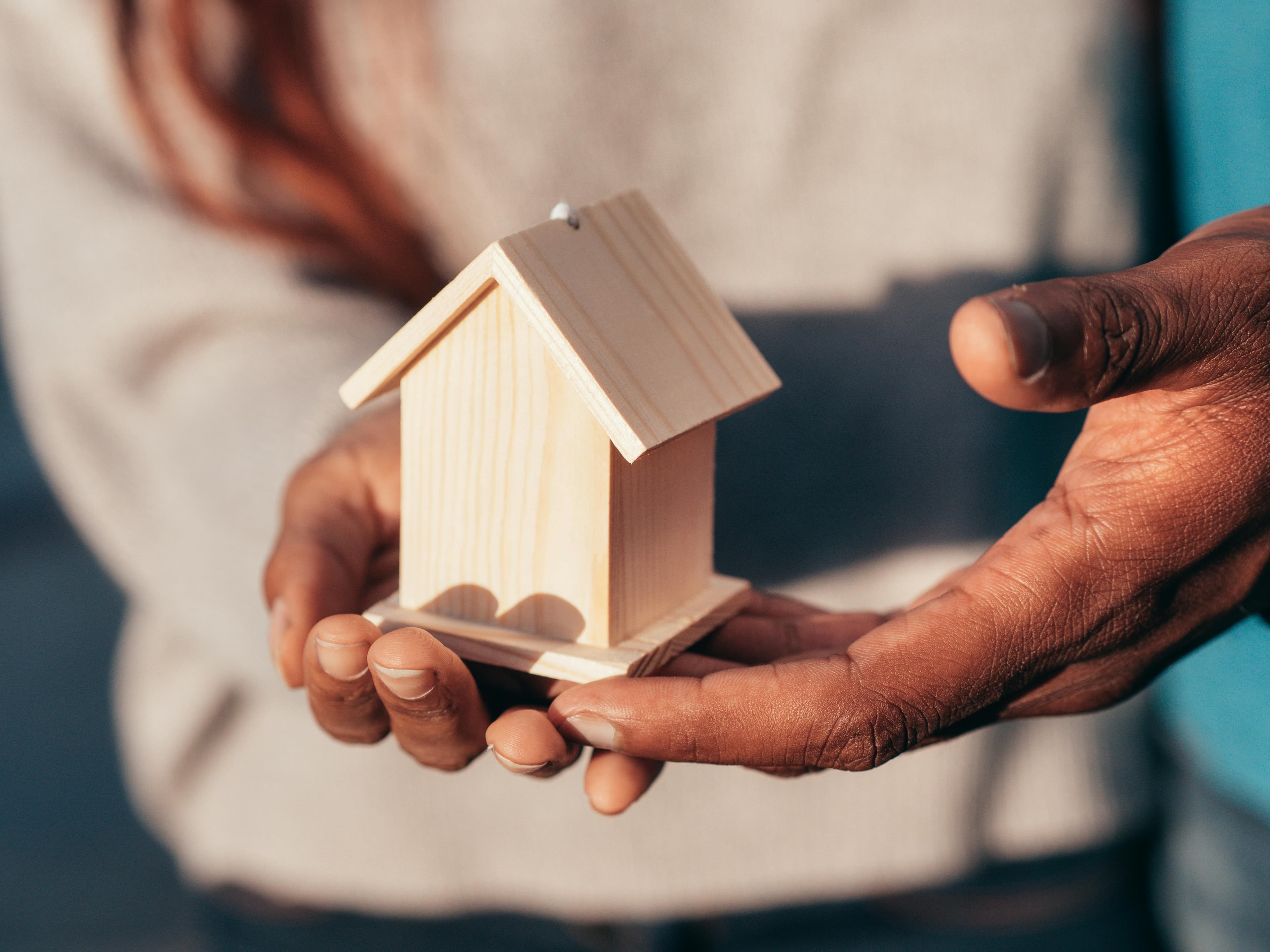 Two hands holding a wooden model of a house.