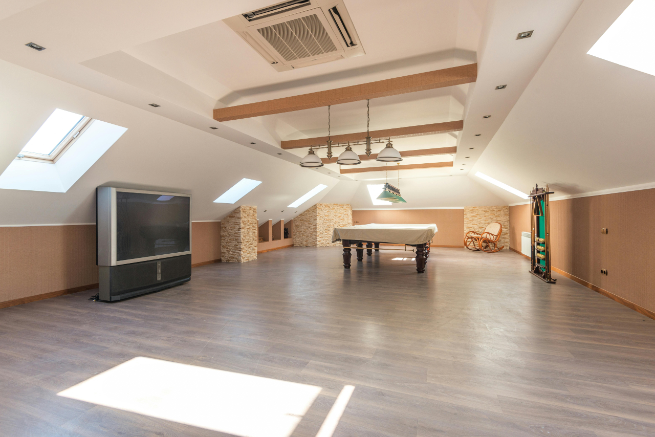 Spacious attic room with a pool table under skylights, a TV, and sitting area.