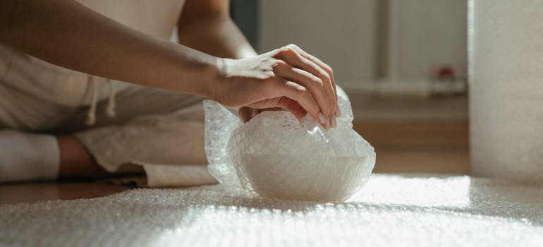 a woman wrapping a glass in bubble wrap