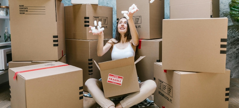 a woman sitting in front of a pile of boxes throwing packing peanuts in the air