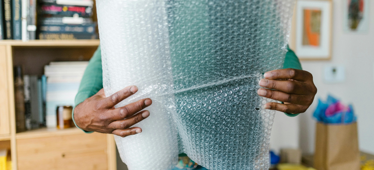 Close-up of hands carefully wrapping a pool table component in bubble wrap to move a pool table safely.