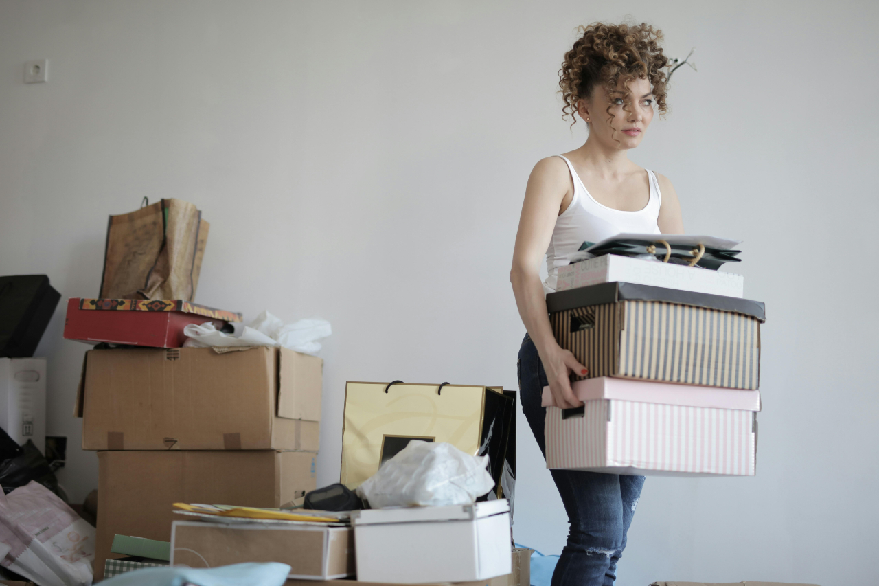 Woman carrying stacked boxes in a room filled with packed items.