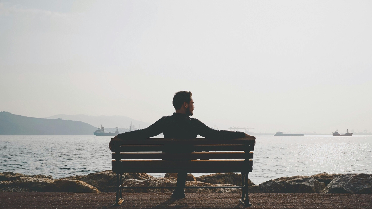 Man Sitting on Bench Near Body of Water