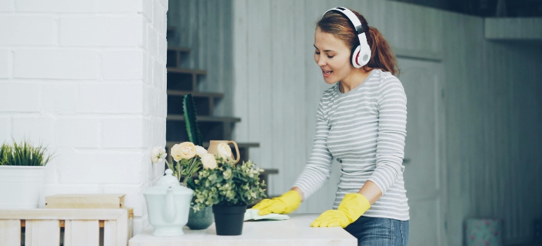 Person wiping surfaces with gloves and headphones representing how to clean a house before you move in.